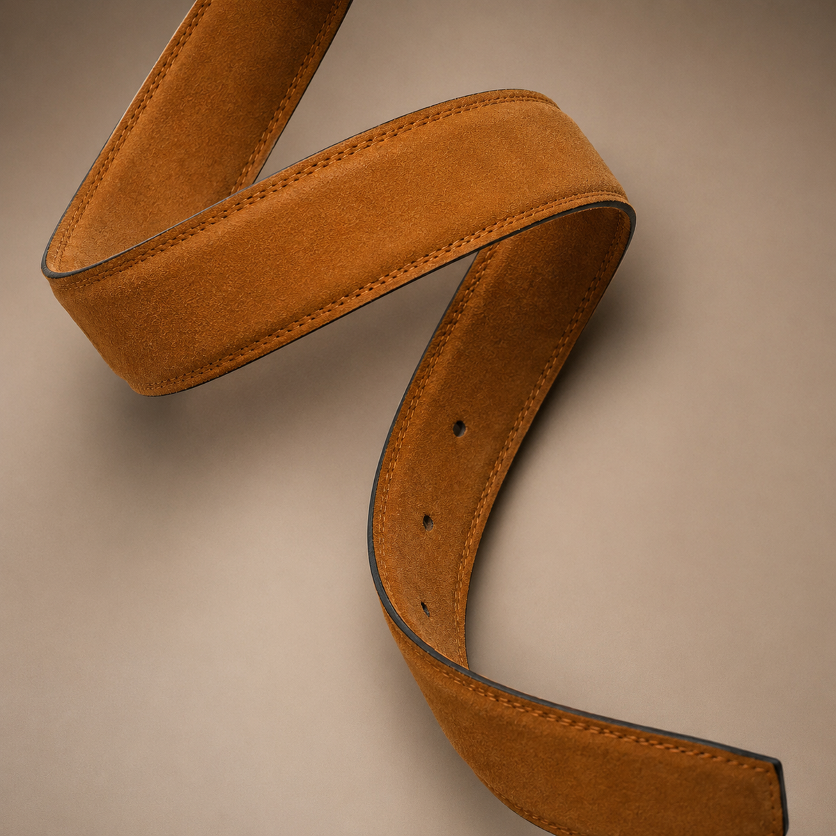 A close-up of a tan suede belt with dark edge trim, arranged in a curved loop on a neutral beige background.